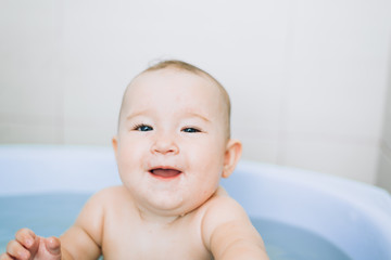 little girl baby is bathed in the blue basin in the bathroom is very fun