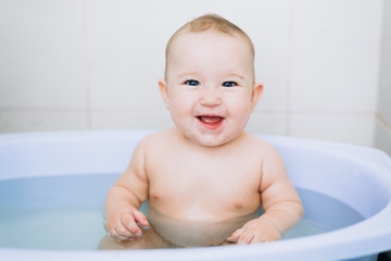 little girl baby is bathed in the blue basin in the bathroom is very fun