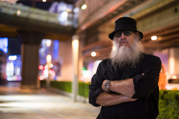 Mature bearded tourist man with arms crossed in the city at night