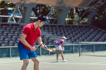 Side view of an Asian tennis player ready to serve at the beginning of a doubles mixed match on a...