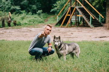 Naklejka na ściany i meble young man showing something to husky dog in park