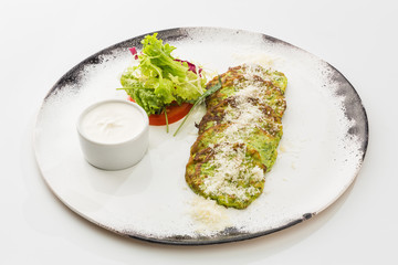 zucchini pancakes with salad and sauce on a plate isolated on white background