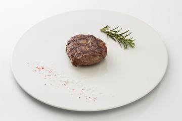 steak with salt and rosemary on a plate isolated on white background