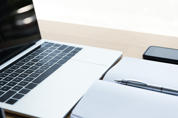 close-up view of blank notebook with pen, smartphone and laptop on table