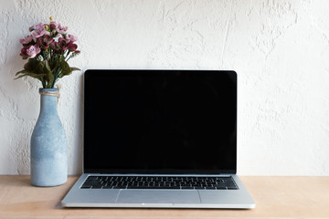 laptop with blank screen and beautiful flowers in vase on wooden table