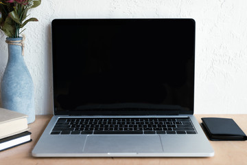 close-up view of laptop with blank screen, smartphone, books and vase on table