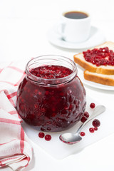 glass jar of cranberry jam on a white table, coffee and toast