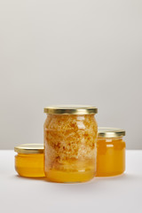 close up view of glass jars with honey on white surface on grey backdrop