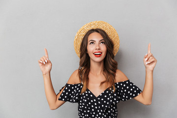 Cute woman wearing hat pointing over grey wall.