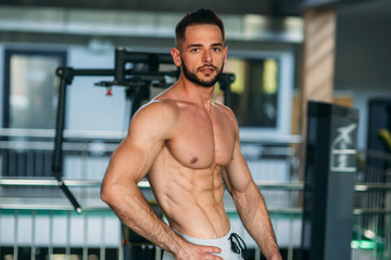 Fototapeta na wymiar Young athlete posing with a torso for photography on a gym background. Bodybuilder, athlete with pumped muscles
