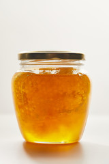 close up view of honey and beeswax in glass jar on white background
