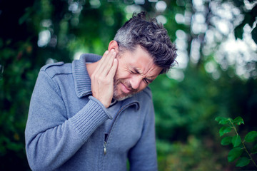 Male having ear pain touching his painful head outdoor