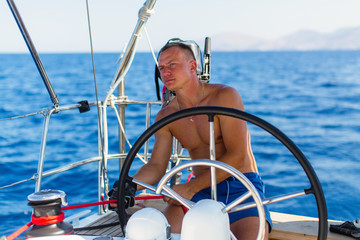 A man skipper runs a sailing yacht on the open sea.