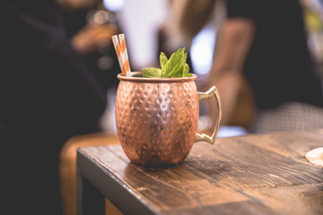 Close up on a copper cup with Moscow Mule cocktail, fresh mint as decoration and a white and orange...