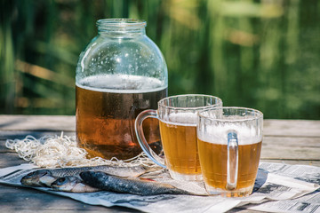 Beer in a jar and in mugs with dried fish on the pier near the river