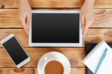 Girl hands with digital tablet and cup of coffee on a wooden table