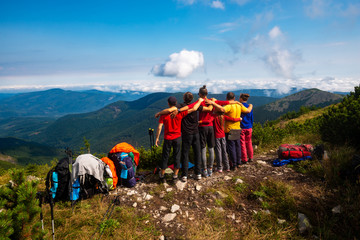 Hikers, friends stand, embracing on a mountain top