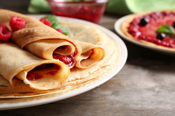 Rolled thin pancakes with sweet jam and berries on plate, closeup