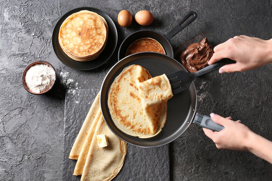 Woman holding frying pan with freshly baked thin pancake over table