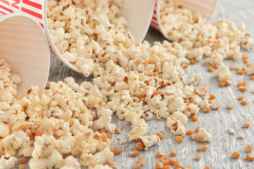 Paper buckets with scattered tasty popcorn on wooden background