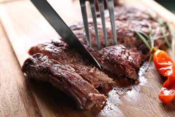Cutting grilled steak on wooden board, closeup