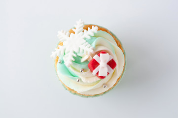 Fototapeta na wymiar New year or christmas green cupcake top view with whipped cream, decorated with a snowflake and red box on white background.