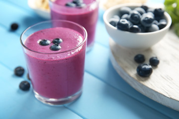 Glass with tasty blueberry smoothie on color wooden table