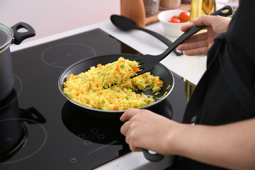 Woman cooking rice with vegetables in kitchen
