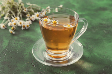 Cup of delicious camomile tea on green table