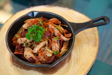 Sizzling hot and spicy Spaghetti alla salsiccia with sausage and bacon in a black cast iron pan on a wooden board. Simple classic Italian meal. Perfect for lunch. Natural light. Selective focus.