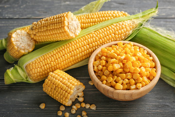 Bowl with corn kernels and fresh cobs on wooden table