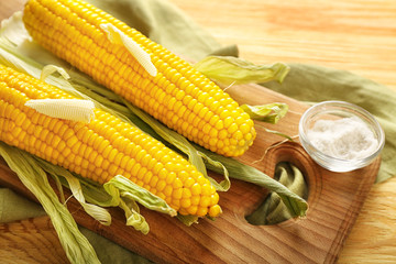 Board with tasty corn cobs, butter and salt on wooden table