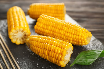 Slate plate with tasty corn cobs on table, closeup