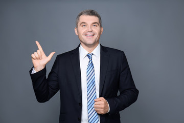 Handsome businessman with raised index finger on grey background
