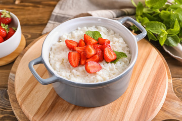 Pot with delicious rice pudding and strawberry on board