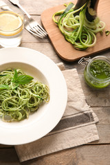 Plate of spaghetti with zucchini and pesto sauce on wooden table