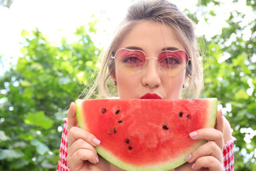 Beautiful young woman eating slice of tasty watermelon outdoors