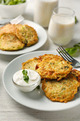 Plate with zucchini pancakes and sauce on wooden table