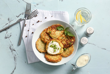 Plate with zucchini pancakes and glass of water on table