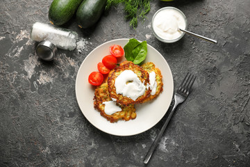 Plate with zucchini pancakes and sauce on grunge table