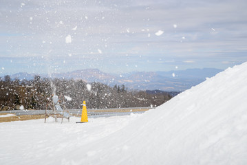 Wide detail of pipe connected to snowmaking machine spraying snow into the air and onto the slopes...