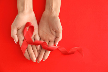 Woman holding red ribbon on color background. AID awareness concept