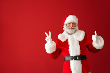 Fototapeta na wymiar Portrait of Santa Claus showing thumb-up and victory gesture on color background
