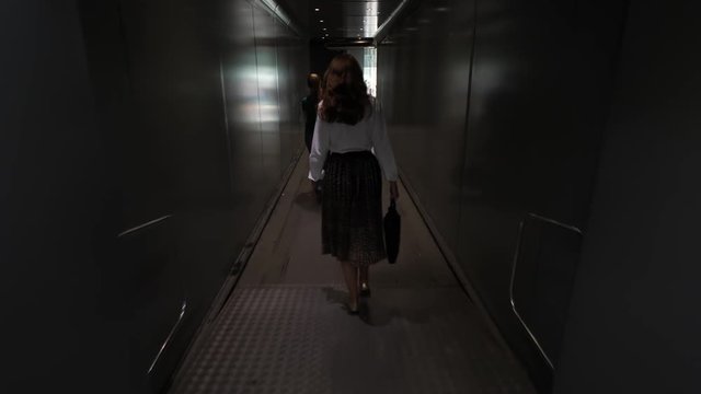 Passanger woman go out of airplane, walk with hand baggage in aerobridge