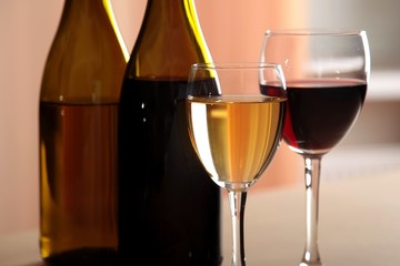 A glass of white wine and a glass of red wine next to bottles of