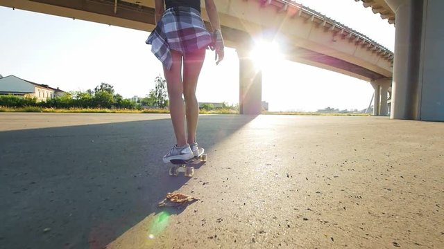 Beautiful girl rides a skateboard under the bridge in the sun, in the frame of the leg