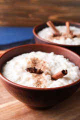 Delicious rice pudding with cinnamon and anise in bowl on wooden board, closeup