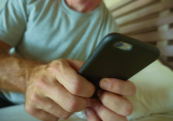 crop face portrait with close up hands holding mobile phone of young man at home bedroom using internet social media app on smartphone networking