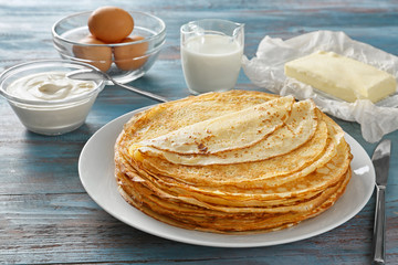 Plate with tasty thin pancakes and ingredients on wooden table