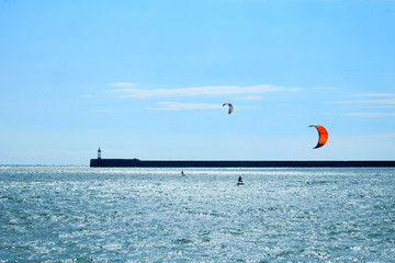 The Newhaven lighthouse and harbour wall are in the middle with a blue sunlit sea in the foreground and blue and white clouds in the background horizontal format lots of space idea for text space.